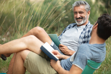 men in camping chairs reading a book