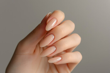 Closeup to woman hands with elegant neutral colors manicure. Beautiful nude manicure on long almond shaped nails. Nude shade nail manicure with gel polish at luxury beauty salon - obrazy, fototapety, plakaty