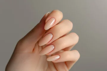 Tuinposter Closeup to woman hands with elegant neutral colors manicure. Beautiful nude manicure on long almond shaped nails. Nude shade nail manicure with gel polish at luxury beauty salon © vejaa