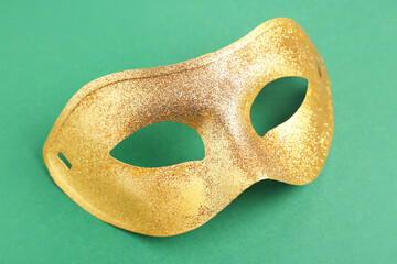 Shiny golden carnival mask for Mardi Gras celebration on green background