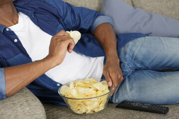 cropped view of man eating snacks while watching tv