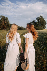 The image features two women wearing white dresses standing outdoors in a grassy field under a cloudy sky. 5630
