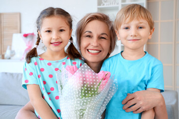 Mature woman with tulips hugging her little grandchildren at home. International Women's Day