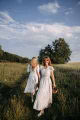 Fototapeta na wymiar The image features two women in white dresses standing in a field of tall grass under a cloudy sky 5634.