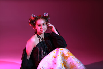 Young woman in colored dress and black jacket sitting on the floor on pink background