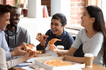 Excited diverse millennial students laugh and joke enjoying tasty pizza from takeaway delivery...