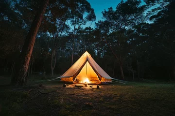 Fotobehang Night and warm light exposure of an illuminated bell tent surrounded by trees and a small camp fire at night, outdoor camping lifestyle © Alizeh