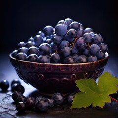 Blue grapes in a plate. Dark grapes in porcelain plate on a black background. Bunch of grapes with leaves. Summer berries. Sweet delicious grapes.