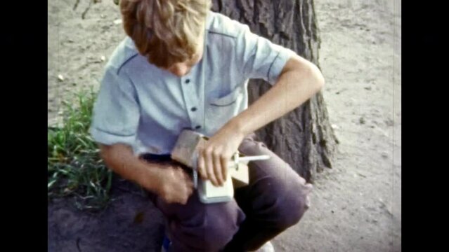 Happy boy sharpens pencils with mechanical sharpener. Joyful childhood. New school purchases. Smiling schoolboy teenager with office supplies, pencil sharpener. Vintage color film. Retro archive 1980s
