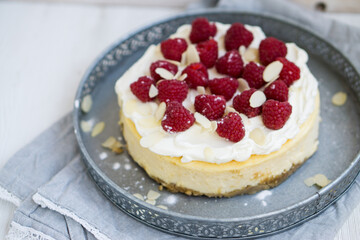 Classic New York cheesecake with whipped cream on top and fresh raspberries on white wooden background close up selective focus