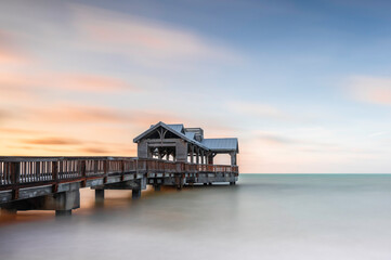 A wooden pier, reaching out into a totally smooth, calm ocean, at sunrise, as colour creeps into the sky.