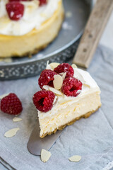 Classic New York cheesecake with whipped cream on top and fresh raspberries on white wooden background close up selective focus