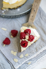 Classic New York cheesecake with whipped cream on top and fresh raspberries on white wooden background close up selective focus