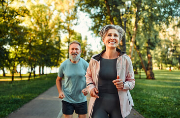 Sport training on fresh air. Front view of positive old man and woman with grey hair enjoy nature...