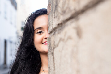 Close-up portrait of half the face of a beautiful woman, with black hair, outdoors leaning against a cement wall.