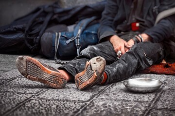 Homeless person laying on the ground, wearing battered, broken shoes