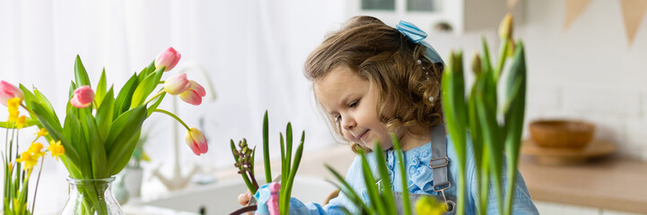 Cute little girl in a pretty blue dress doing home gardening in the kitchen, taking care about flowers and plants. Domestic life, cozy atmosphere, family time, development, hobby, leisure. Banner - Powered by Adobe