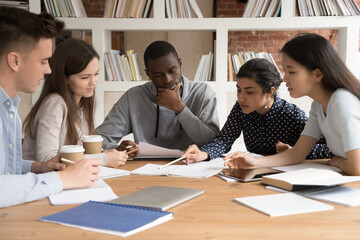 Concentrated multiracial students at shared desk work at group project share ideas at meeting,...