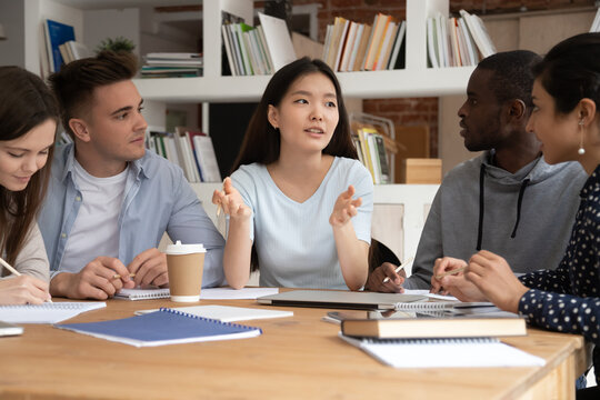 Focused international students sit at desk discuss school educational project brainstorm together, concentrated multiethnic young people study at shared table consider work on paperwork in classroom