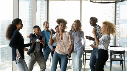 Corporate party. Overjoyed group of multicultural students employees dancing in modern office having fun achieving success in teamwork. Excited mixed race colleagues friends celebrate business reward - obrazy, fototapety, plakaty