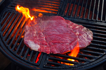 Traditional raw barbecue flanksteak steak as close-up on a charcoal grill with fire