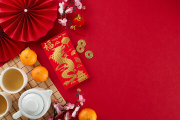 Meaningful chinese New Year tea ceremony idea. Top view shot of money envelope, tea crockery, tangerines, traditional chinese decor on red background with congratulations space