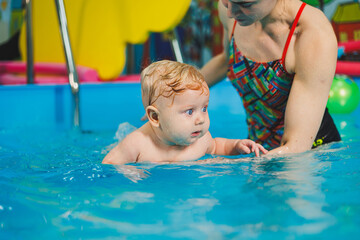 Teaching a newborn boy to swim in a pool with a coach. Baby swimming courses. The child swims in the pool