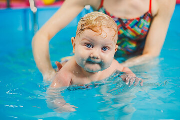 Fototapeta na wymiar Teaching a newborn boy to swim in a pool with a coach. Baby swimming courses. The child swims in the pool