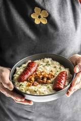 The hands of a senior home cook hold a plate with a national Slovak dish - Bryndzove Halusky.