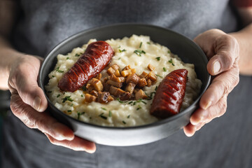 The hands of a senior home cook hold a plate with a national Slovak dish - Bryndzove Halusky.