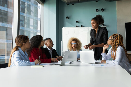 Young diverse multiethnic business team gather on briefing in modern office under lead of afro american female boss. Skilled black woman ceo hold meeting at boardroom speak set tasks to staff members