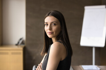 Confident beautiful young Latin company leader woman office portrait. Serious female business coach, project manager standing in boardroom with arms folded, looking at camera