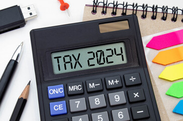Word Tax 2024 on the calculator. Business and tax concept. alculator, coins, book, form, and pen on...