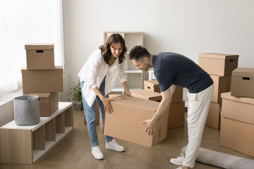 Happy busy couple of home owners unpacking cardboard boxes, carrying paper shipping packages,...
