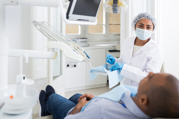 Dentist in uniform is examinating man on the chair