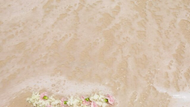 White and pink tropical flower lei in shape of heart washed by warm ocean foamy wave. Love concept, St Valentines Day, Wedding day background.Love symbol in shape of flower heart laying on sandy beach