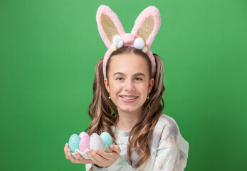 Happy Easter. Funny cute girl with Easter bunny ears and colorful Easter eggs on green background....