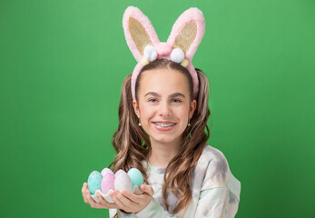 Happy Easter. Funny cute girl with Easter bunny ears and colorful Easter eggs on green background. Copy space.