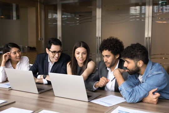Happy multiethnic business colleagues sharing laptop at meeting table, watching online project video preview, talking on group video call, smiling, discussing work application, software for job - Powered by Adobe