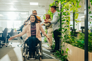 Woman who uses a wheelchair being pushed in an office chair by a male colleague