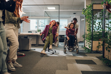 Hispanic woman and a woman with disability participating in an office chair race - obrazy, fototapety, plakaty