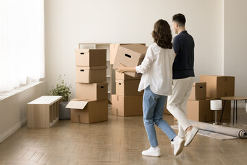 Young couple moving into new apartment after successful mortgage, carrying cardboard packages,...