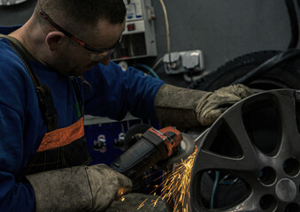 Mechanic in a car service works with a wheel rim with an angle grinder wearing safety glasses