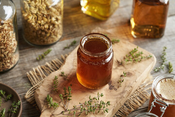 A jar of herbal syrup with fresh thyme on a table - obrazy, fototapety, plakaty