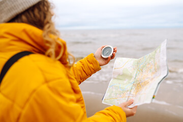 Traveler explorer young woman holding compass and a map in her hands on the beach near the sea....