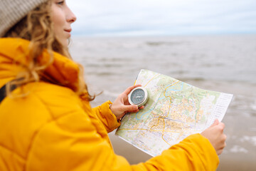Traveler explorer young woman holding compass and a map in her hands on the beach near the sea....
