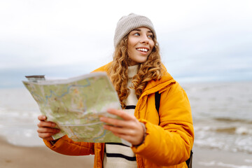 Traveler explorer young woman holding compass and a map in her hands on the beach near the sea....