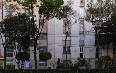 Classically styled apartment building, behind a tree-lined avenue in the afternoon.