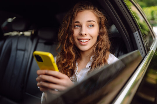 Young woman uses a smartphone while sitting in the back seat of a car.  The concept of business, technology, travel, online communication. Taxi.