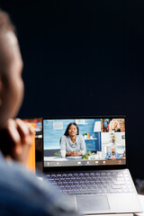African American woman video conferencing with colleagues at home. Female freelancer collaborating online and discussing work using a laptop in a living room office setup.